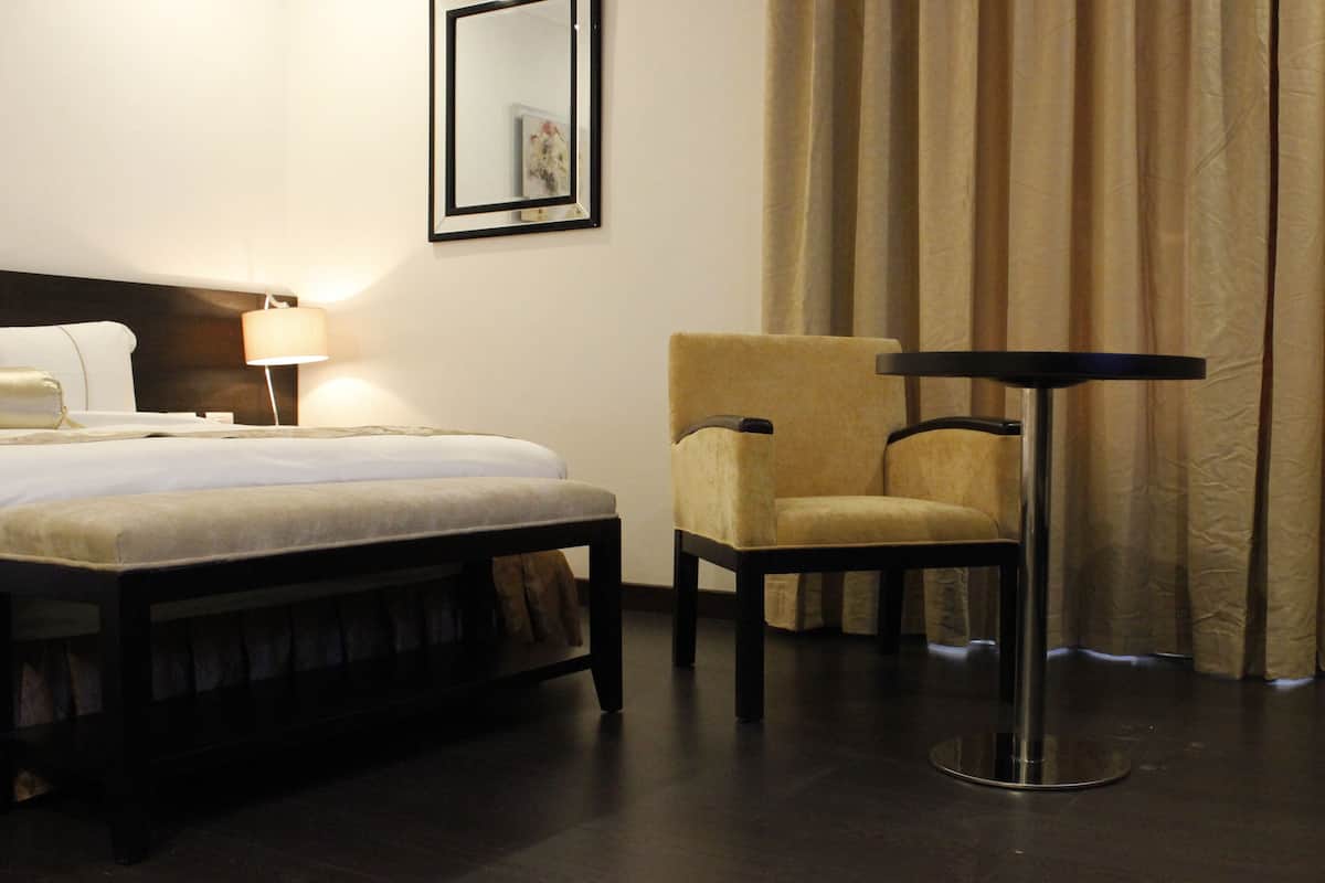 A hotel room with a bed, a chair, a table, and a lamp.