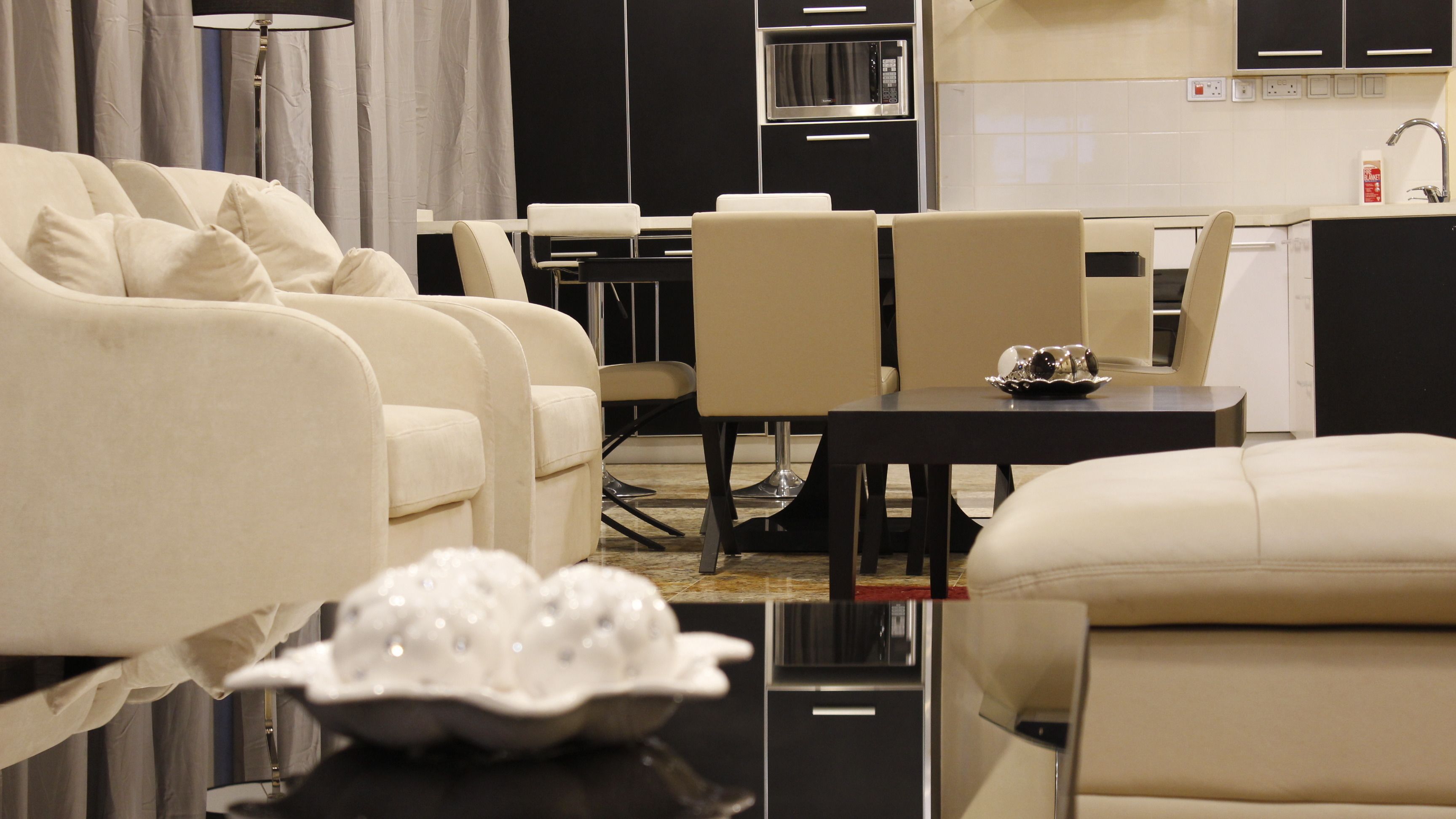 A modern living room with a sofa set, a dining area with a table and chairs, and a kitchen with appliances.