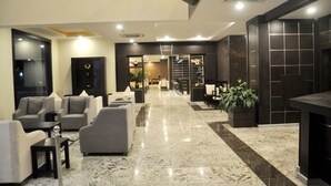Um lobby moderno com piso de mármore, sofás cinzas e um balcão de recepção.
