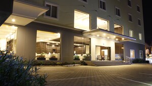 Hotel com design moderno, apresentando um hall espaçoso com área de recepção, diversas opções de assento e entrada bem iluminada.