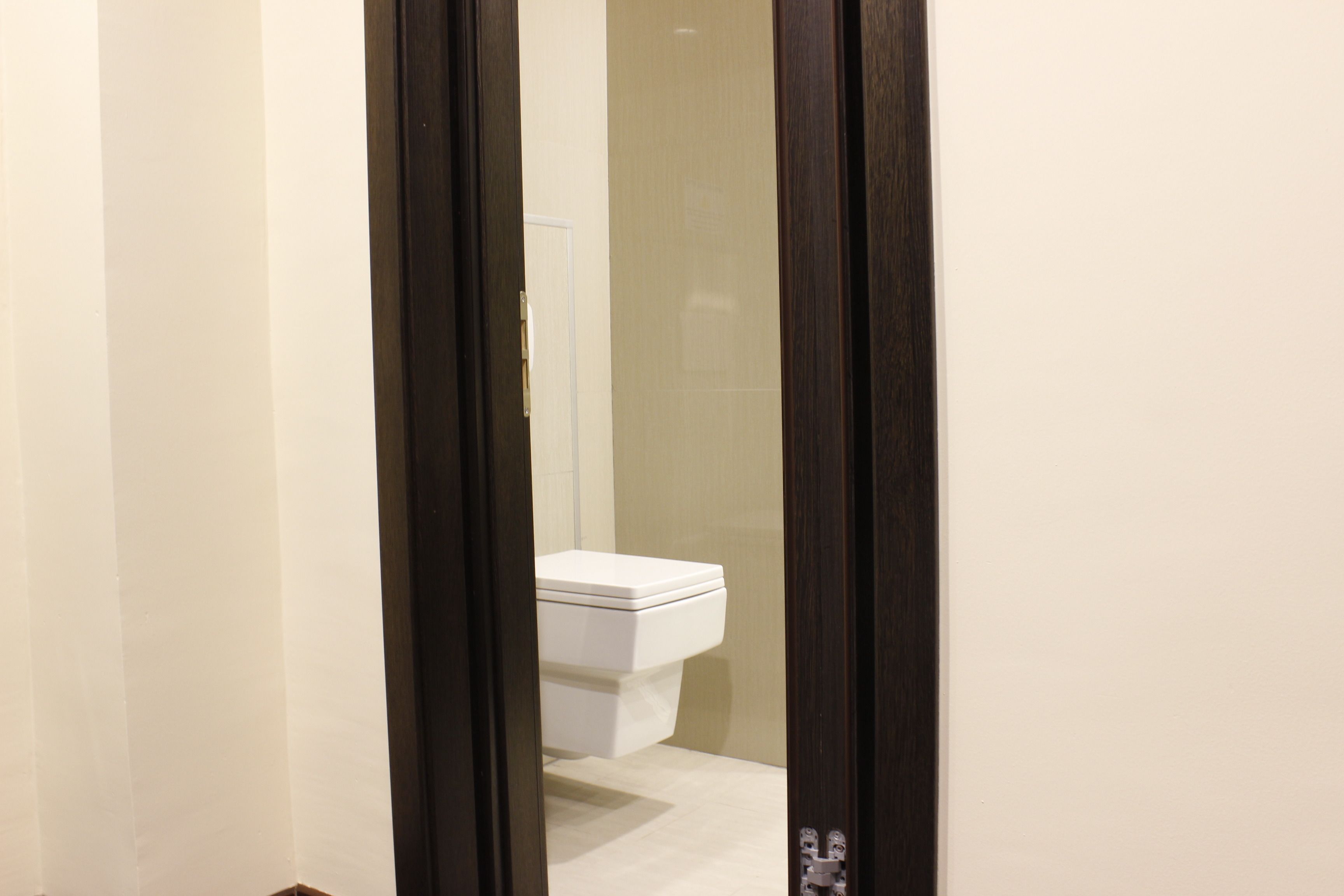 Une salle de bain avec des toilettes blanches, un miroir et un cadre de porte.