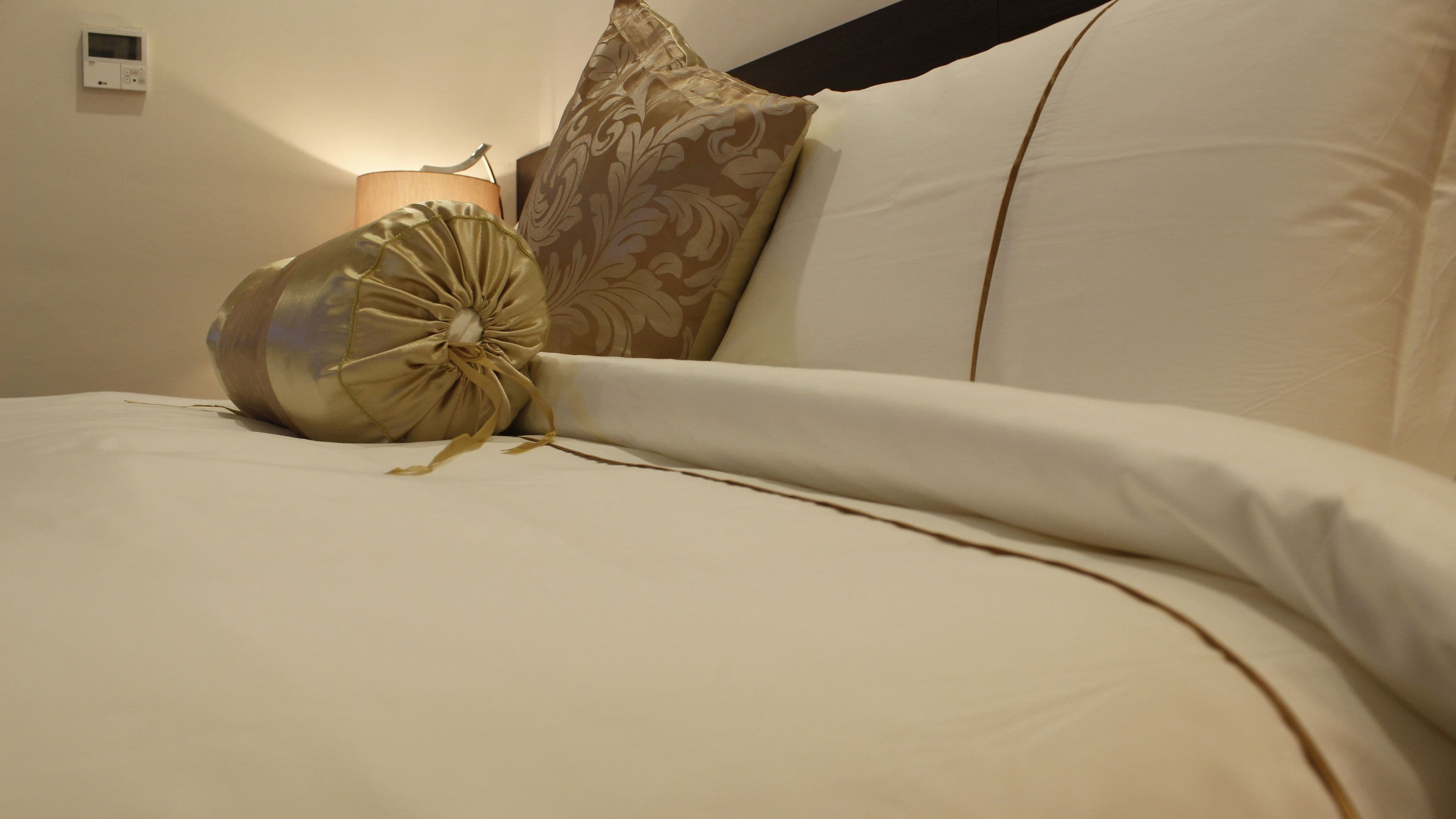 Een net opgemaakt bed met een groot, decoratief kussen en een bijpassend plaid.