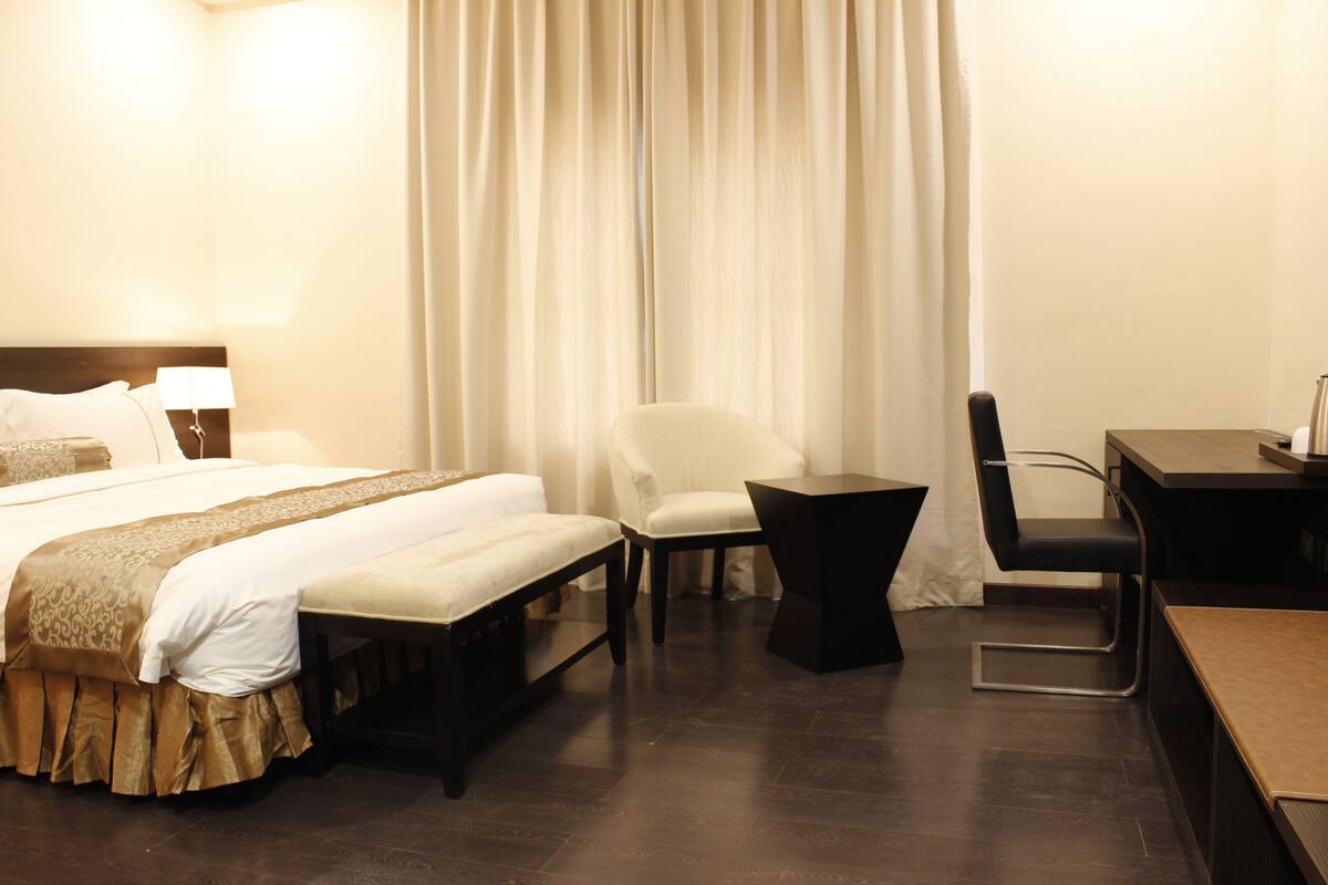 A hotel room with a bed, a desk, a chair, and a window with curtains.