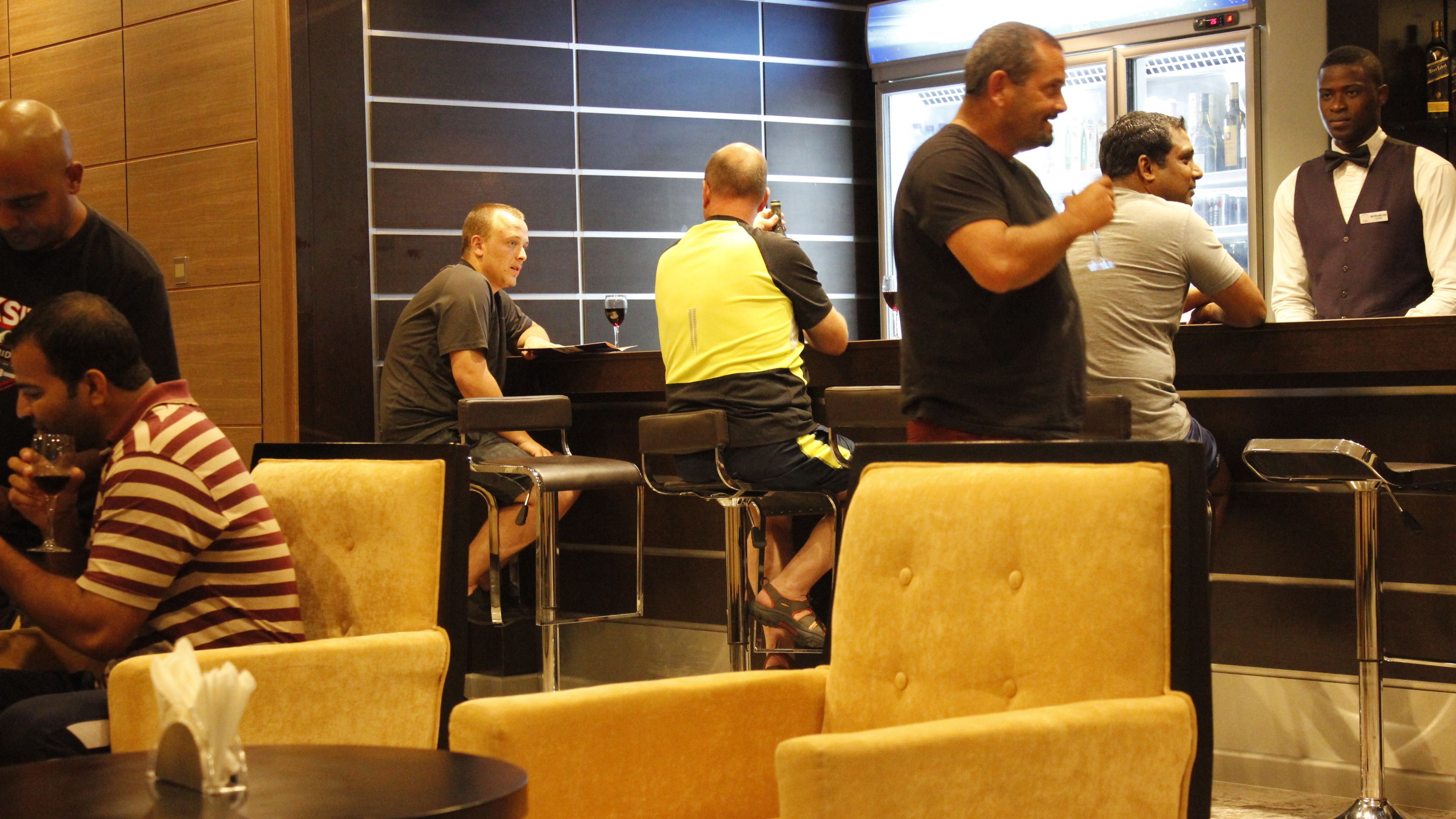 A bar area with seating and a refrigerator stocked with bottles.