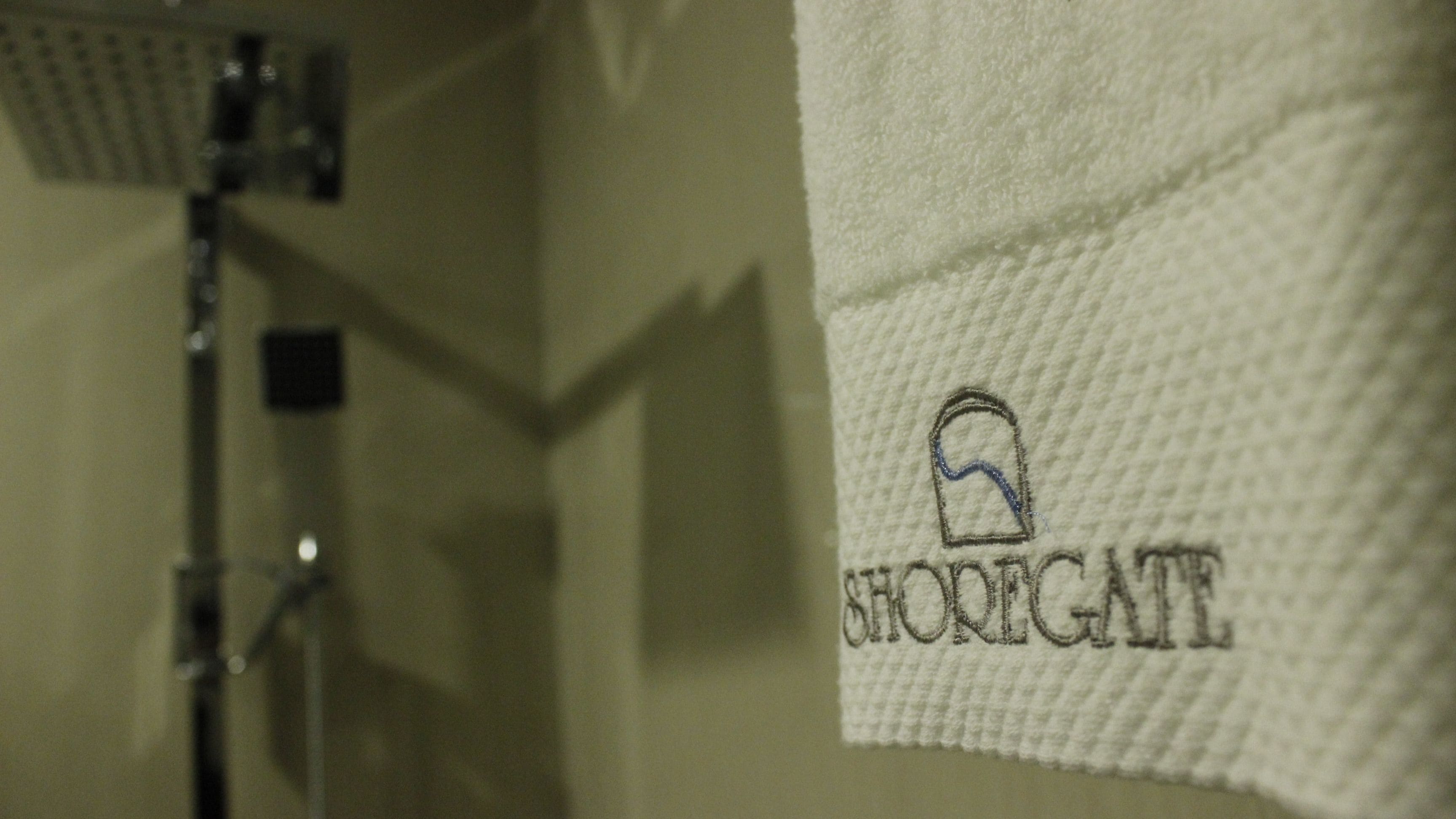 Una toalla blanca con bordado de texto y un logotipo, colgada en un baño.