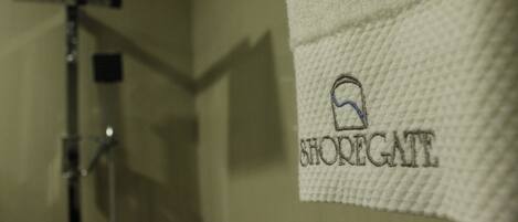 A white towel with embroidered text and a logo, hanging in a bathroom.