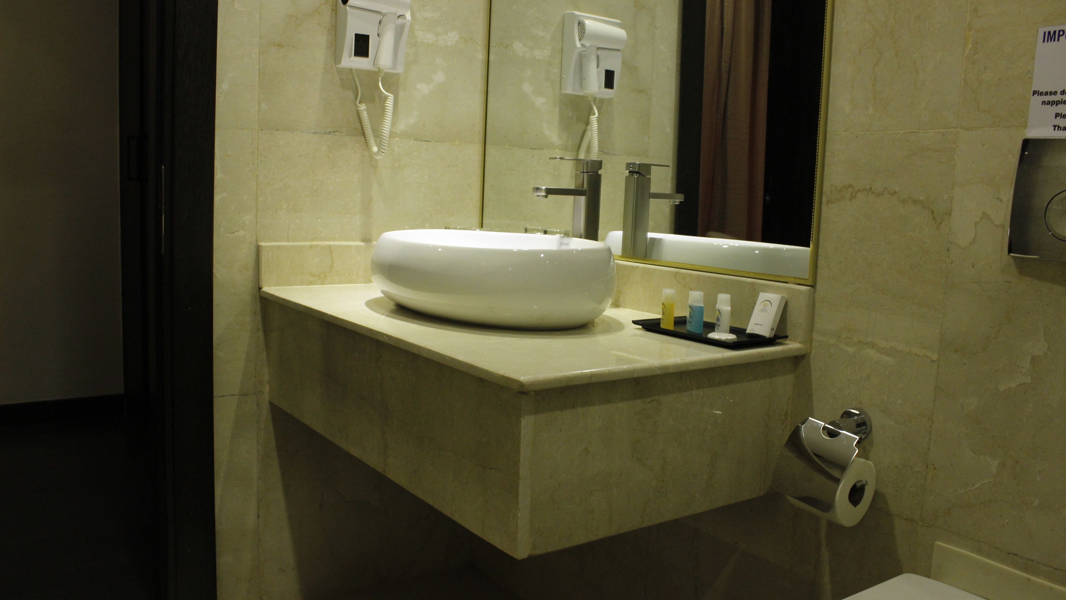 Un baño con un lavamanos grande de color blanco, un espejo, un secador de pelo y artículos de aseo sobre el mostrador.