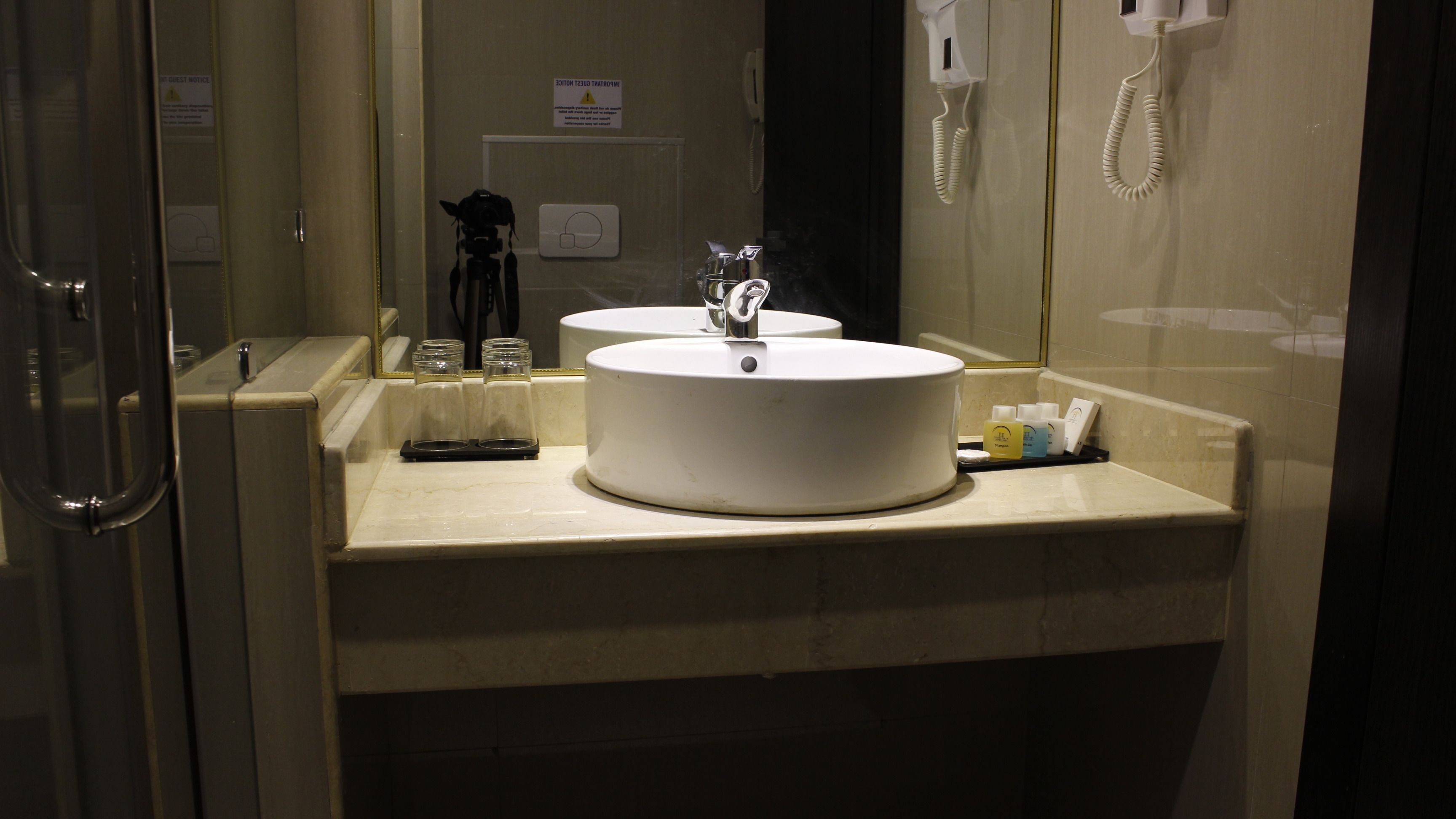 Un baño con dos lavamanos, un espejo, un teléfono y una repisa con artículos de aseo.
