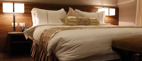A neatly made bed with white linens and a decorative headboard. There are two bedside tables with lamps and a small table beside the bed.