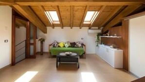 A room with a wooden ceiling, skylights, a sofa with cushions, a small table, and a kitchenette. - La Finestra sul Golfo Affittacamere (La Spezia)