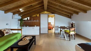 A spacious loft with a high wooden ceiling, a kitchenette, a dining area, and a cozy living space with a green sofa and a coffee table. - La Finestra sul Golfo Affittacamere (La Spezia)