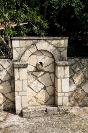 Une construction en pierre dotée d’une entrée en arc de cercle et d’une petite ouverture, entourée d’un mur de pierre et de verdure.