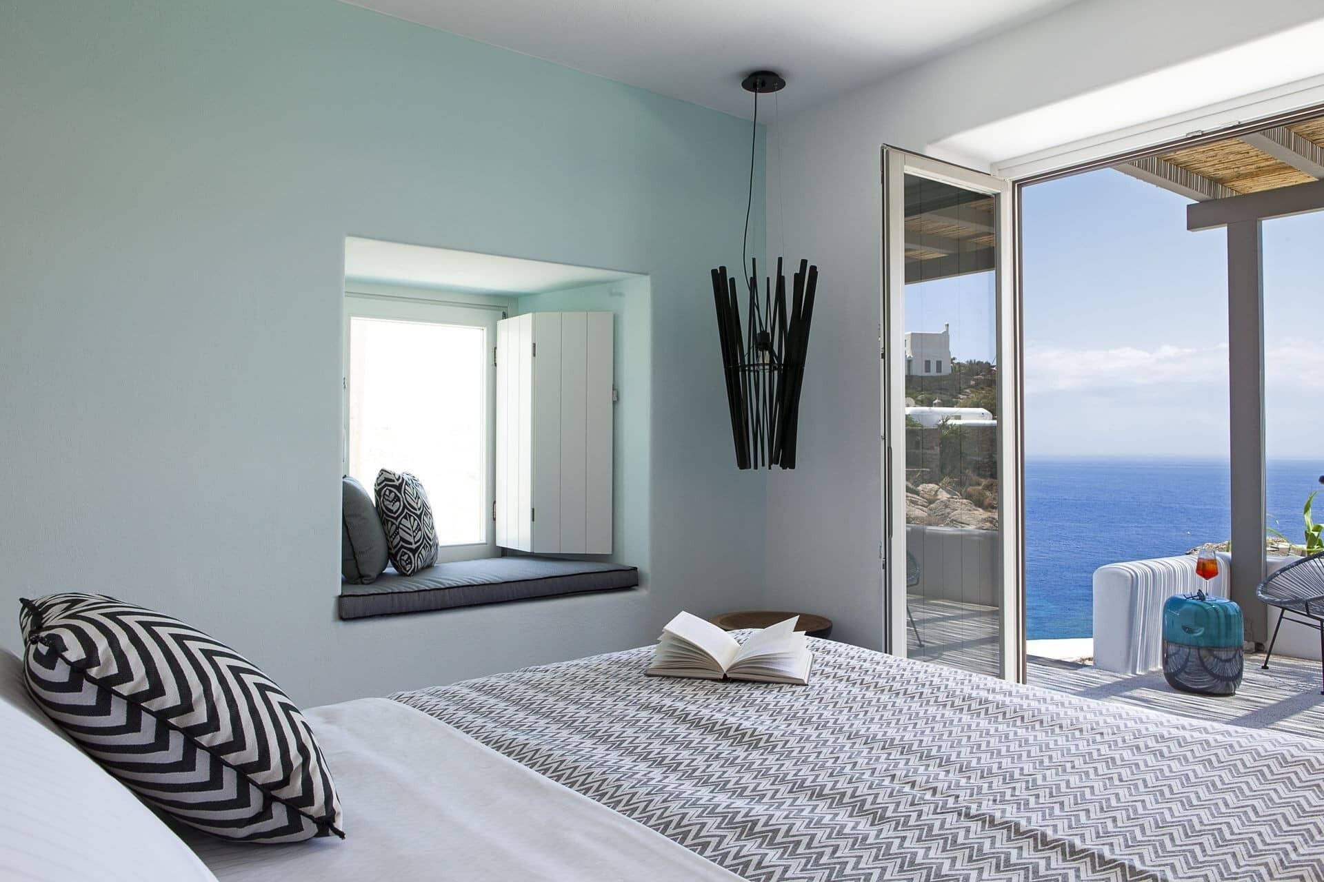 Un dormitorio con cama, ventana, espejo y vista al mar.