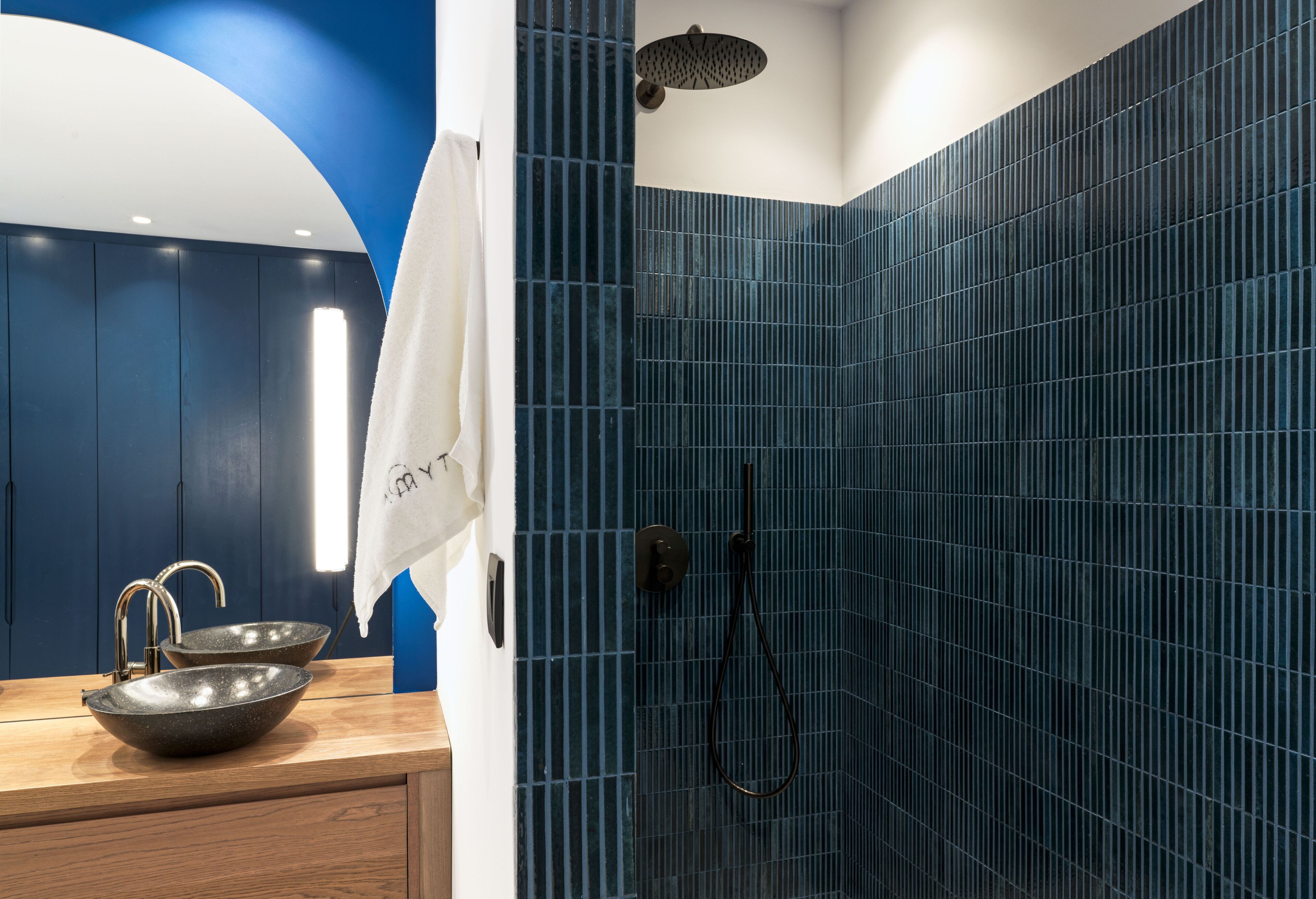 A modern bathroom with a blue tiled shower, a wooden vanity with a bowl sink, and a towel hanging on the wall.