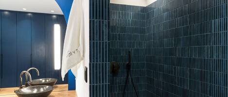 A modern bathroom with a blue tiled shower, a wooden vanity with a bowl sink, and a towel hanging on the wall.