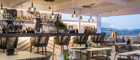 Un restaurante con zona de bar, sillas de mimbre y mesas.