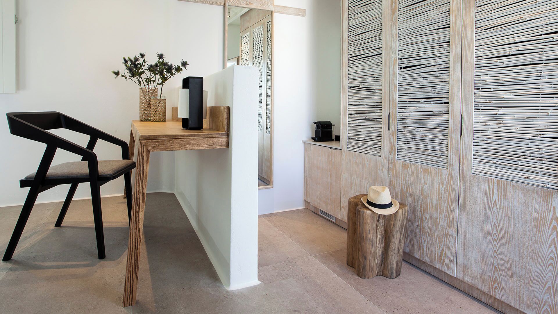 A modern room with a wooden desk, a black chair, a small wooden stool, and a woven basket with plants.