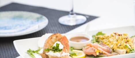 Uma mesa de jantar com pratos de comida, um copo de vinho branco e um jogo americano preto.