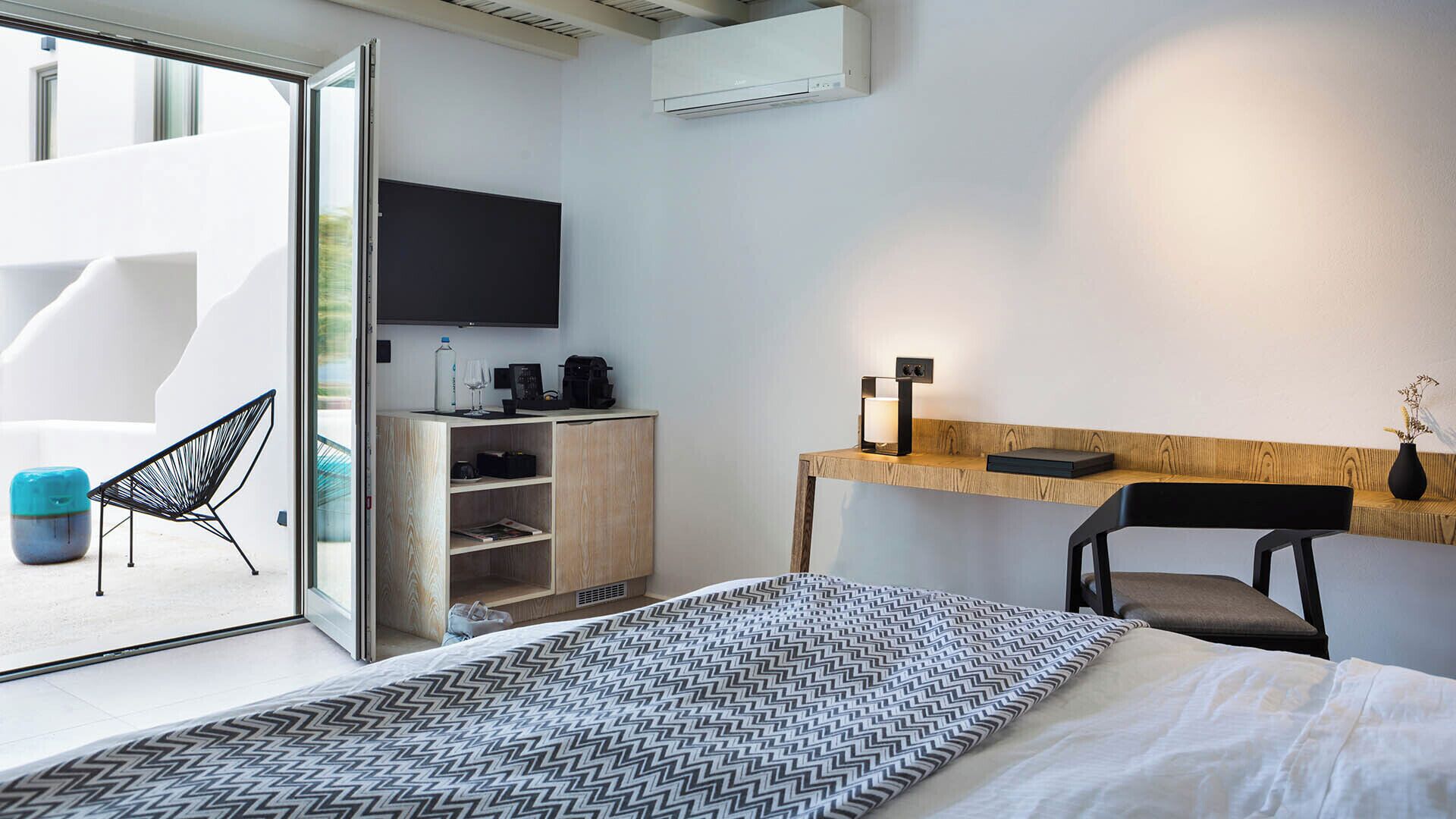 A modern hotel room with a bed, a desk, a chair, a TV, and a balcony.