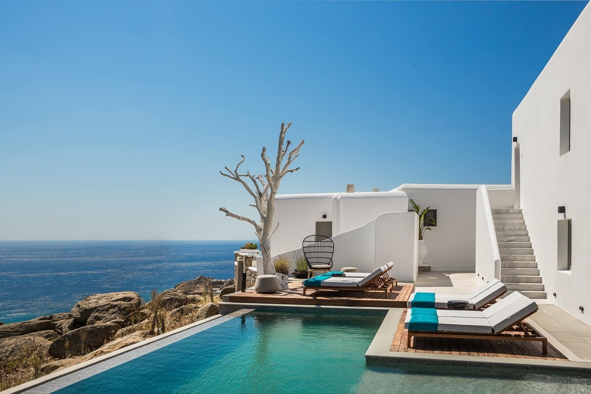 Un espace piscine extérieur moderne, doté de chaises longues et offrant une vue sur la mer.