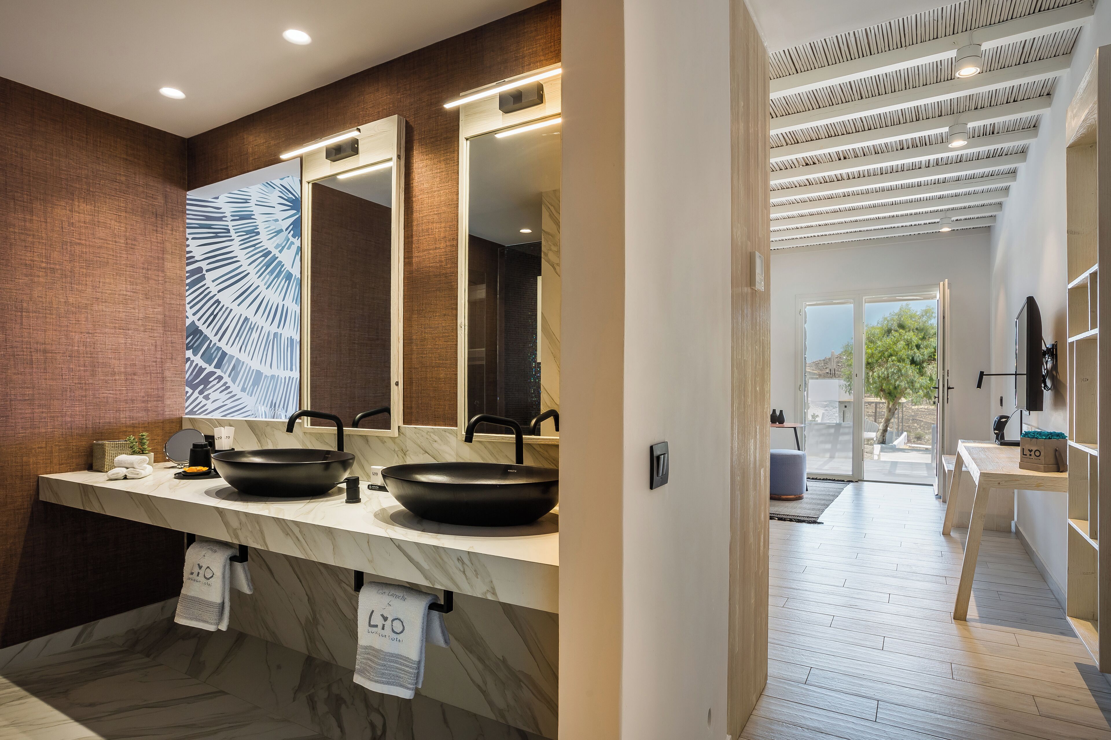 A modern bathroom with two sinks, a large mirror, and a view of the outdoor area.