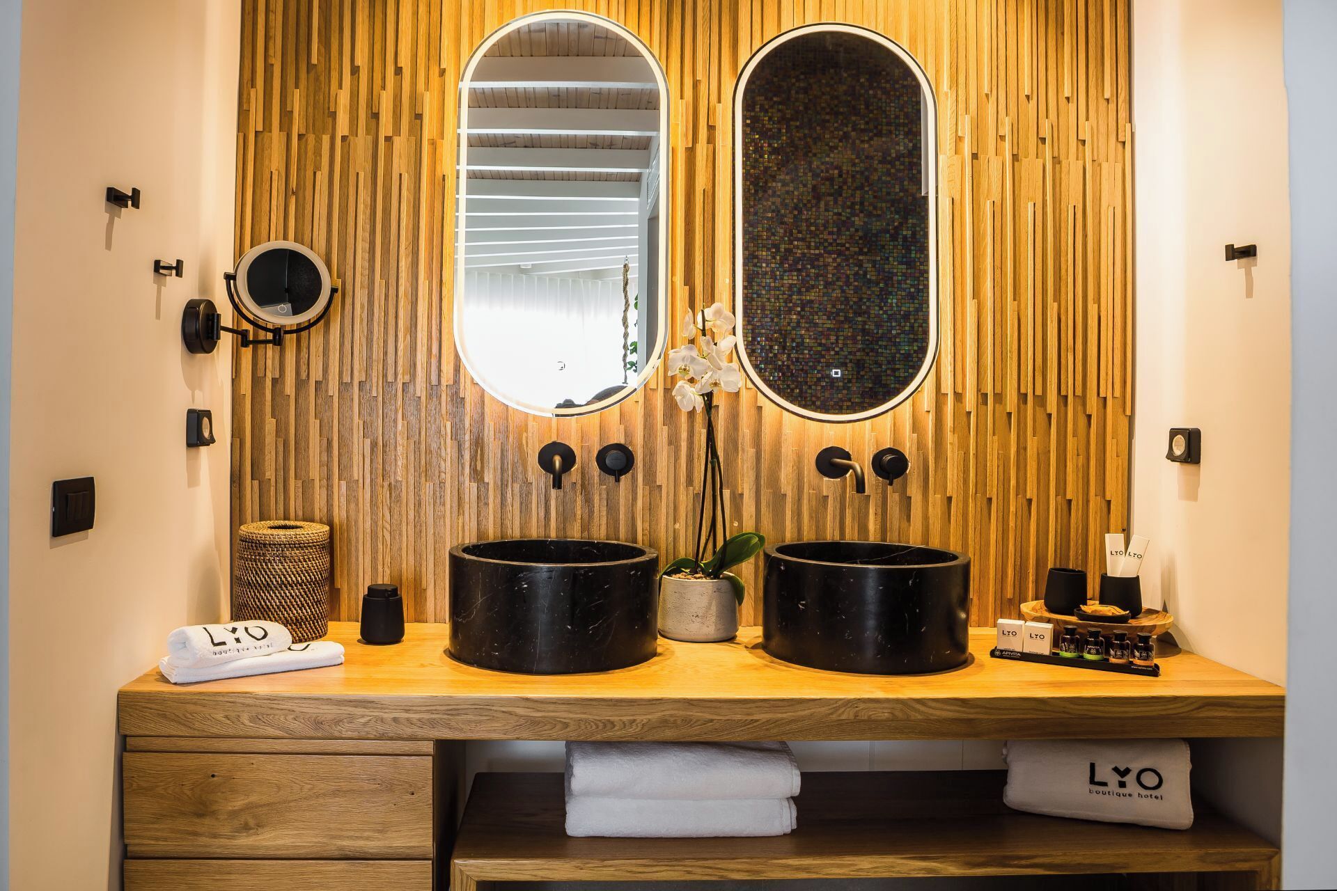 A wooden vanity with two black sinks, a mirror, and a potted orchid.