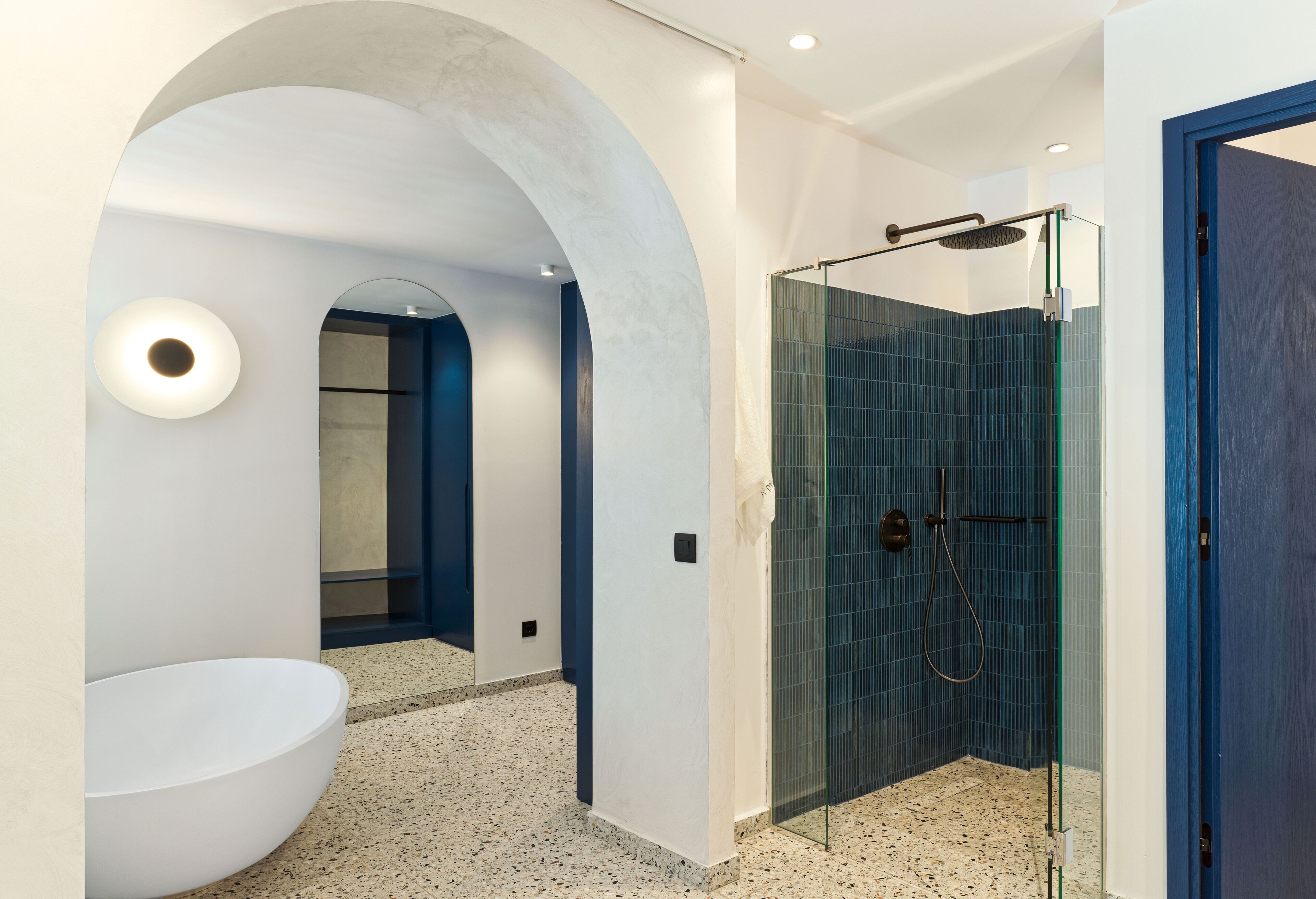 A modern bathroom with a freestanding bathtub, a glass-enclosed shower, and a blue accent wall.