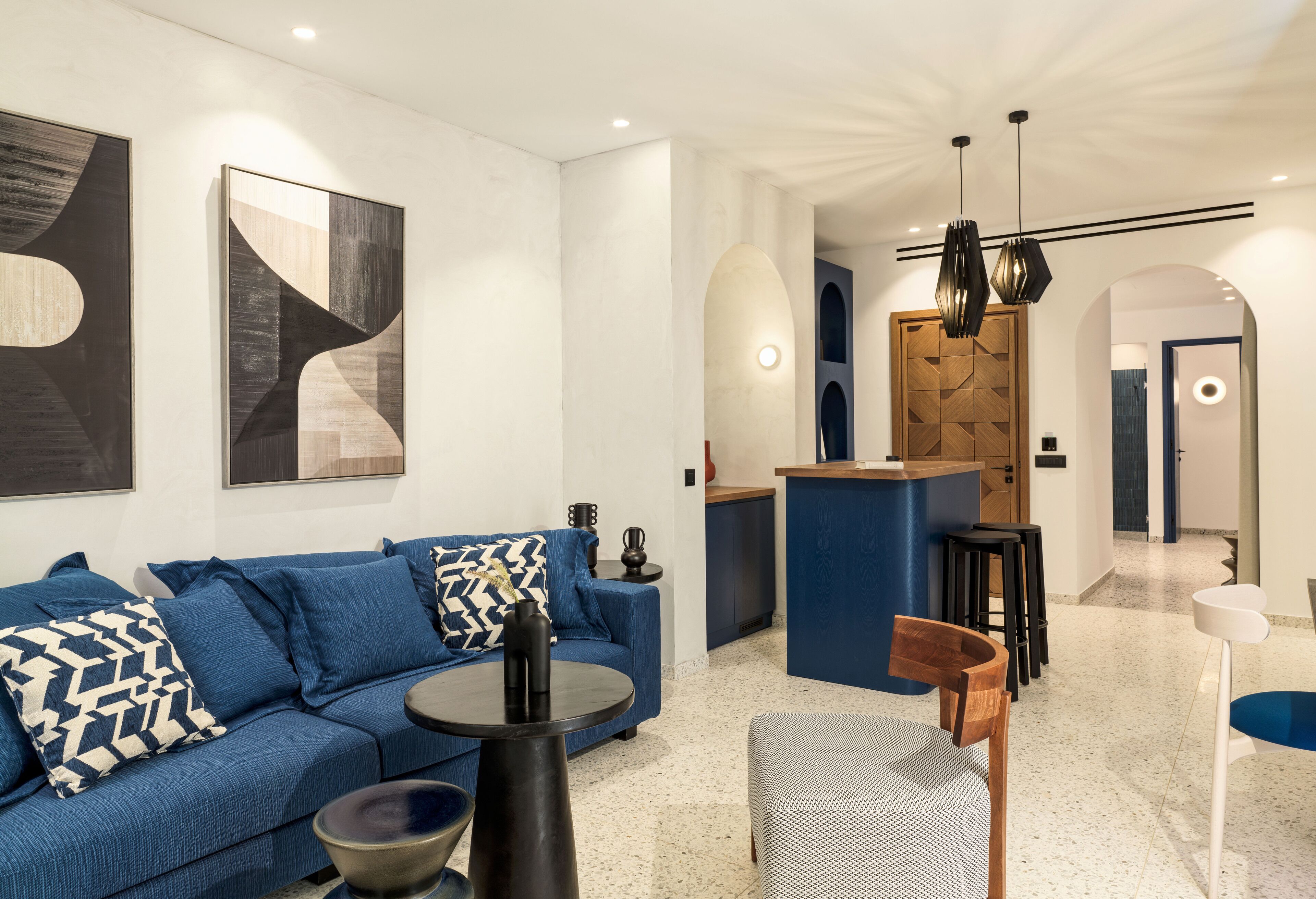 A modern living room with a blue sofa, a coffee table, and a kitchen area with stools.