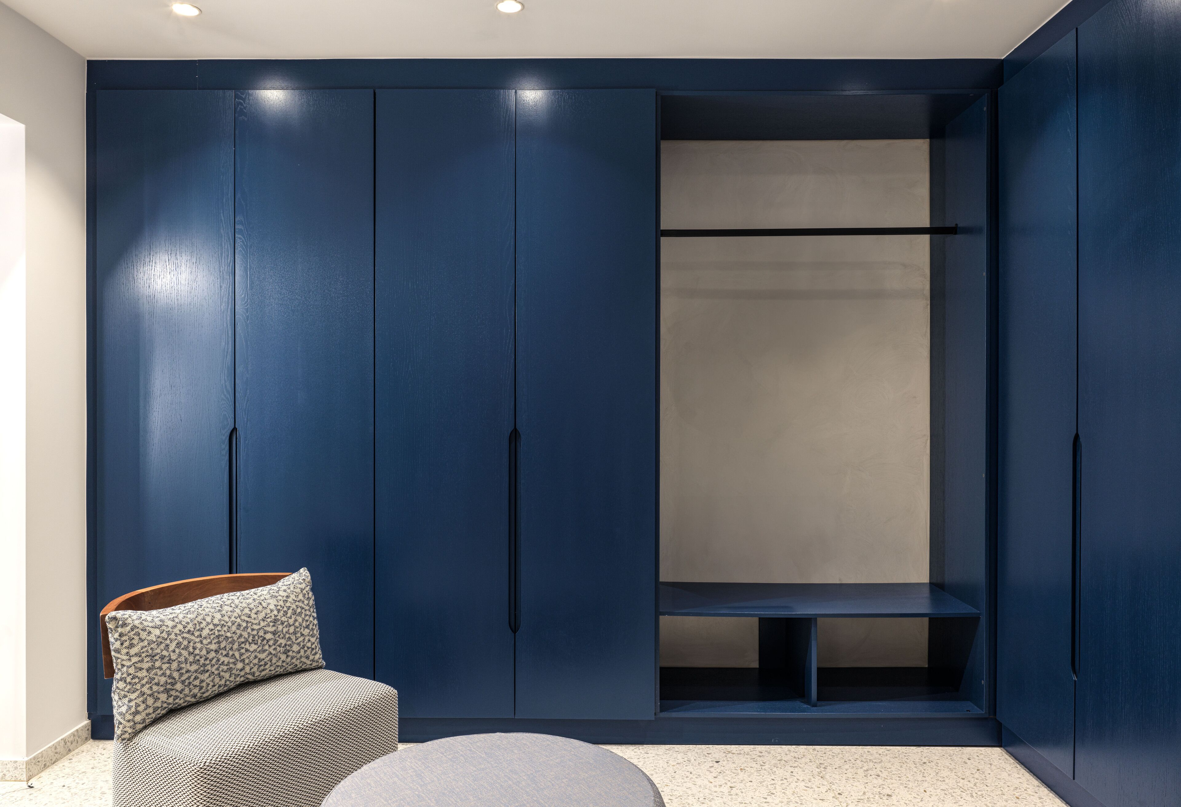 Ein Zimmer mit einem großen blauen Kleiderschrank, einem grauen Sofa mit einem gemusterten Kissen und einem runden Hocker.