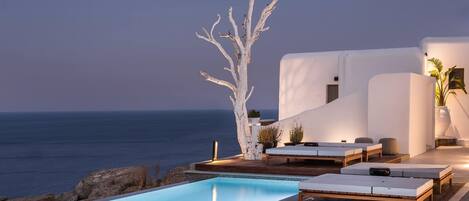 A poolside area with lounge chairs and a white tree sculpture, overlooking the sea.