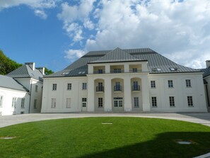 Un grand bâtiment blanc à la façade symétrique, doté de nombreuses fenêtres et d’une entrée centrale.