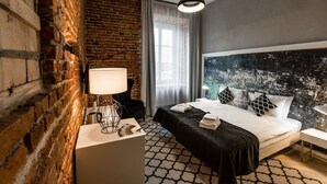 Une chambre d’hôtel moderne avec un mur en briques, un grand lit avec une literie noire et blanche, une table de chevet blanche et un grand tableau abstrait accroché au mur.