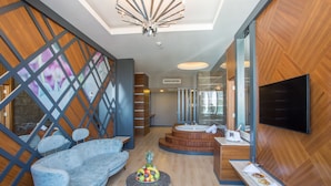 A modern hotel lobby with a blue sofa, a fruit bowl, a TV, and a bathroom with a mirror and sink. - Sensitive Premium Resort & Spa - All Inclusive (Serik)