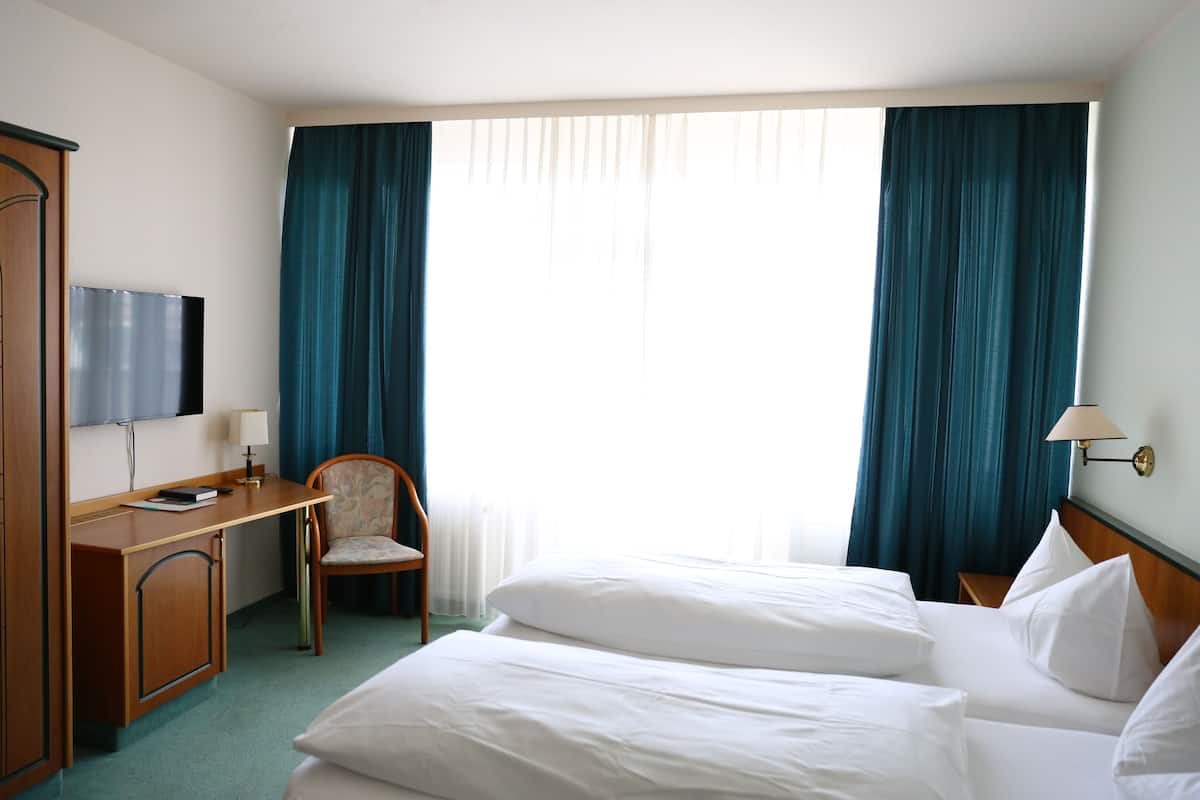 Une chambre d’hôtel avec un lit, un bureau et une chaise, une télévision et une fenêtre avec des rideaux.