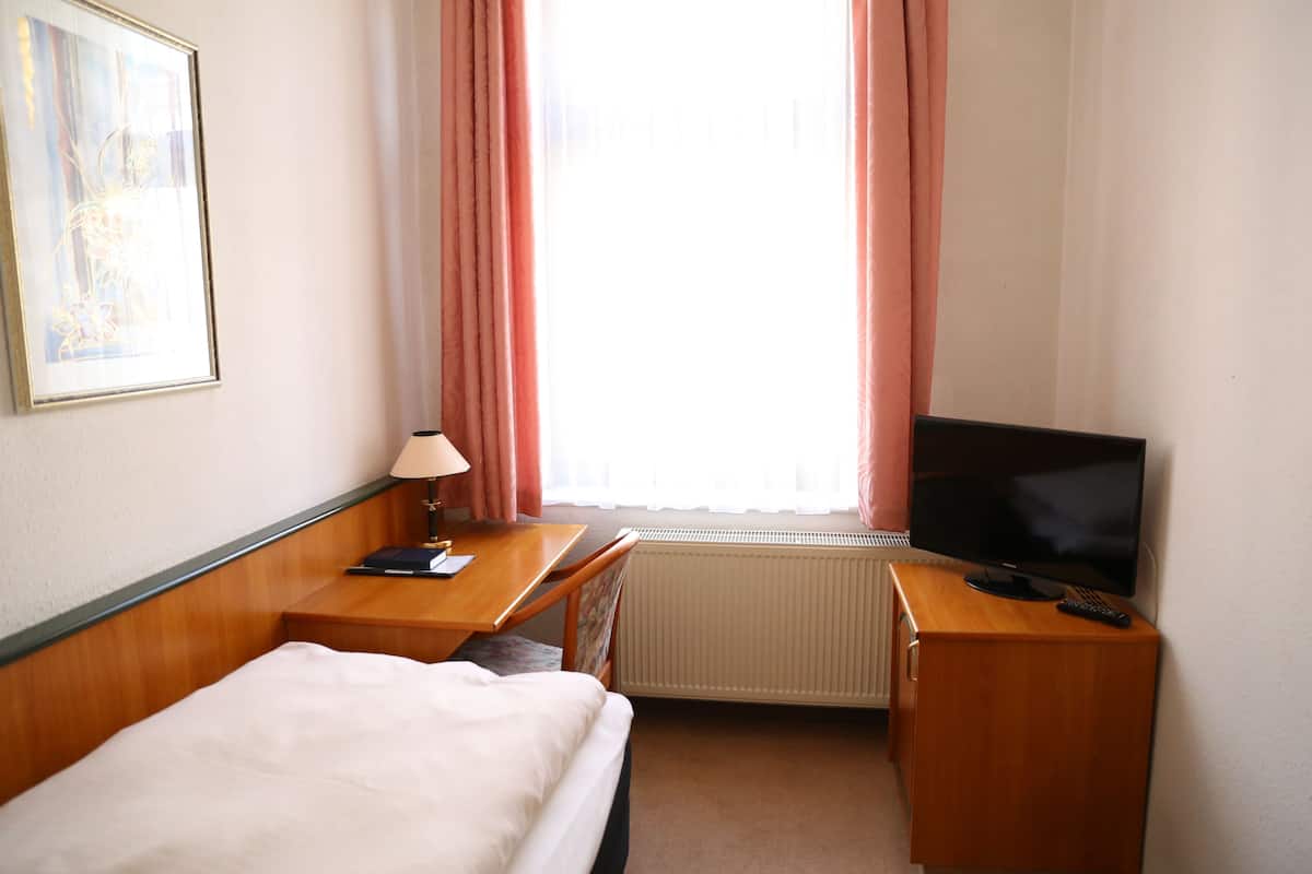 Une chambre d’hôtel avec un lit, un bureau doté d’une lampe, une télévision et un radiateur.