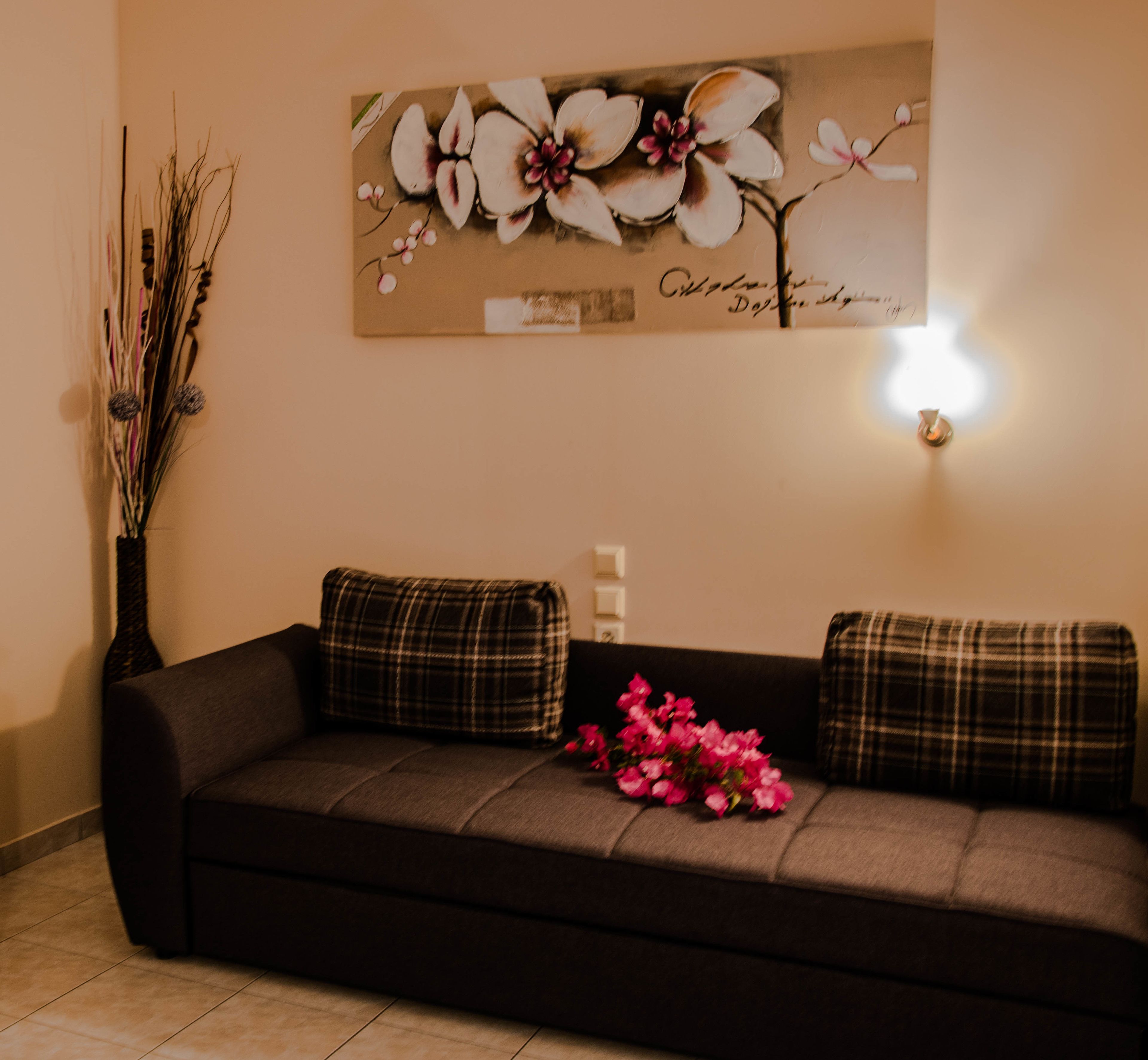 A dark brown sofa with plaid cushions, a vase with branches and pink flowers, and a wall-mounted light.