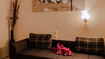A dark brown sofa with plaid cushions, a vase with branches and pink flowers, and a wall-mounted light.