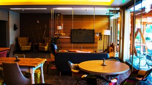 Un ambiente moderno con un tavolo da pranzo in legno, sedie e un divano. C'è una televisione a parete e una finestra con persiane.