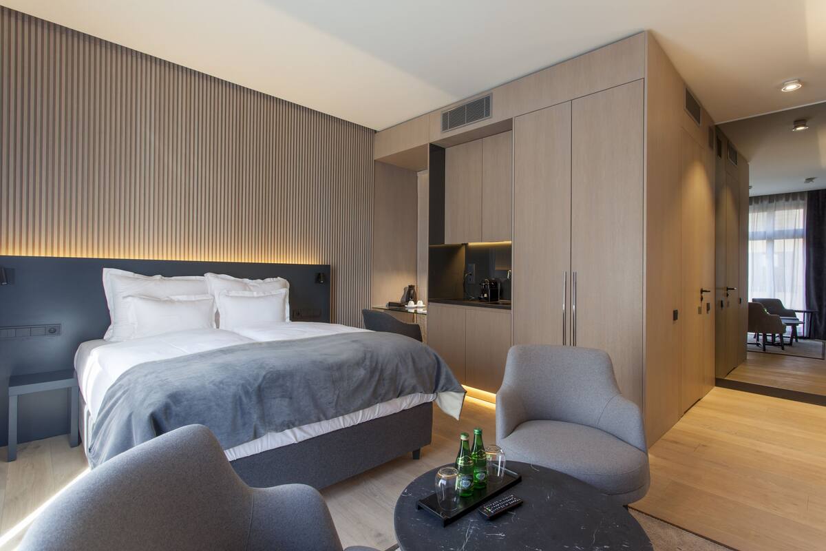 Una habitación de hotel moderna con una cama grande, una zona de estar con una mesa de centro y una kitchenette.