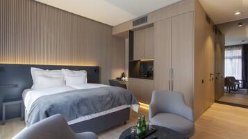 A modern hotel room with a large bed, a seating area with a coffee table, and a kitchenette.