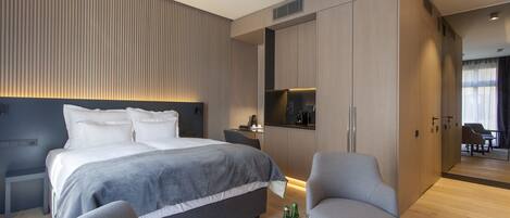 A modern hotel room with a large bed, a seating area with a coffee table, and a kitchenette.