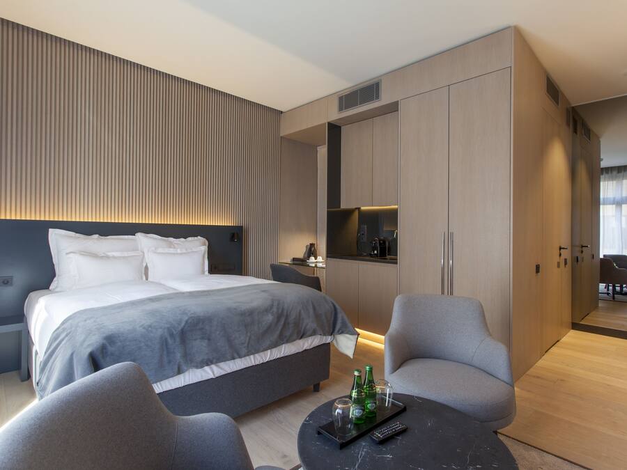 A modern hotel room with a large bed, a seating area with a coffee table, and a kitchenette.