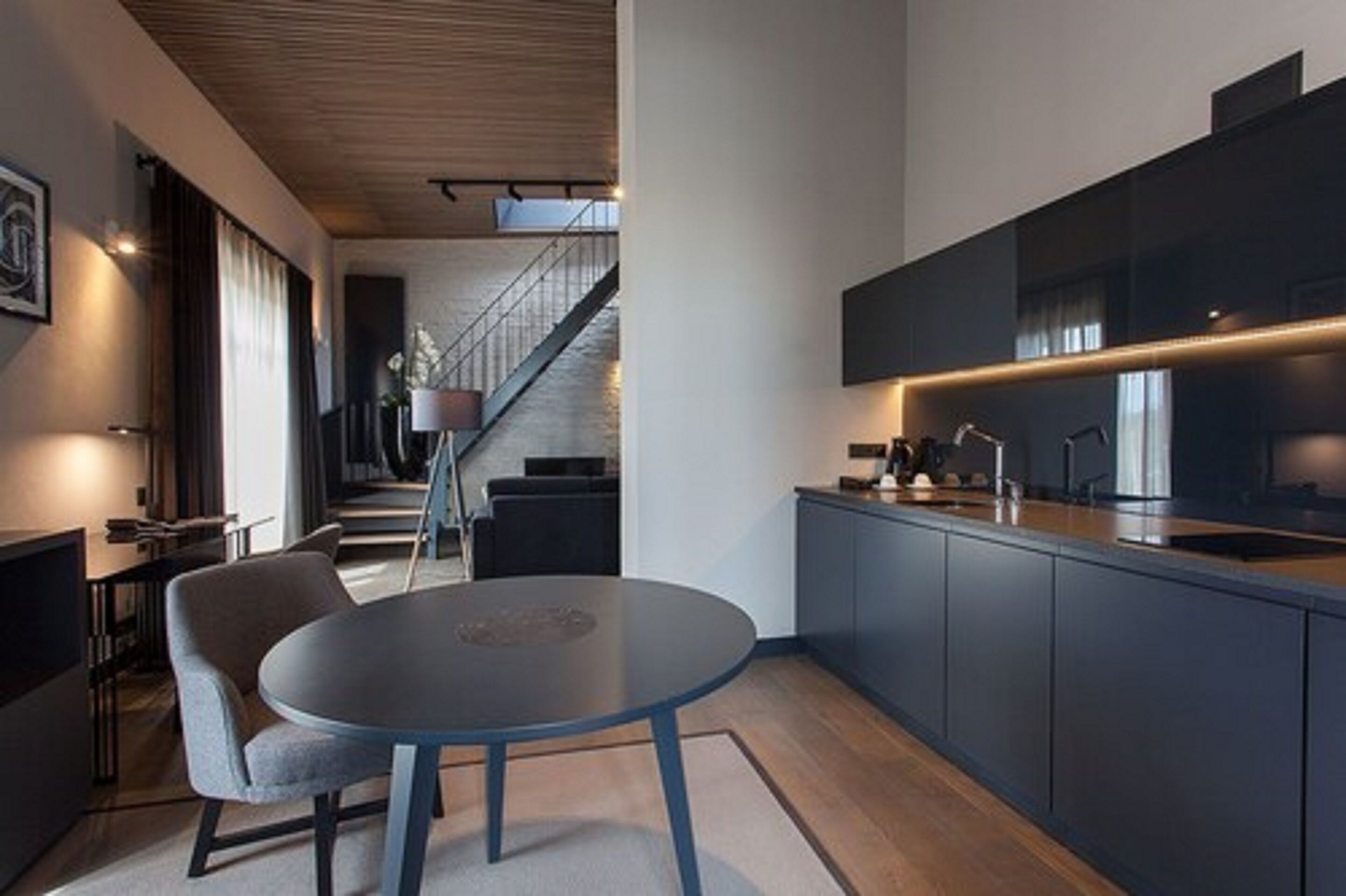 A modern kitchen with dark cabinetry, a round table, and a staircase leading to another level.