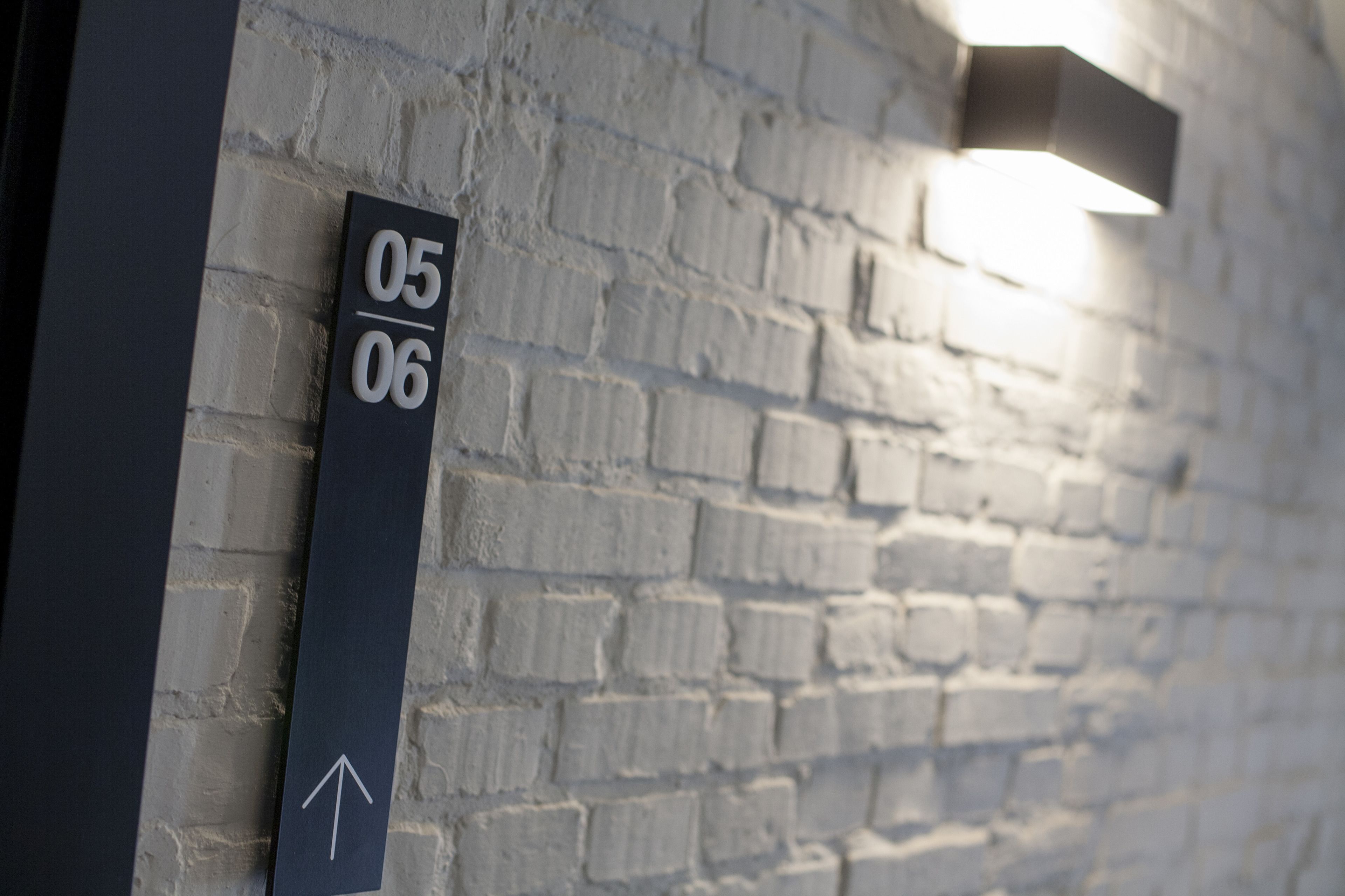 Schild mit den Zahlen „05/06“ und einem nach oben zeigenden Pfeil an einer Backsteinmauer.