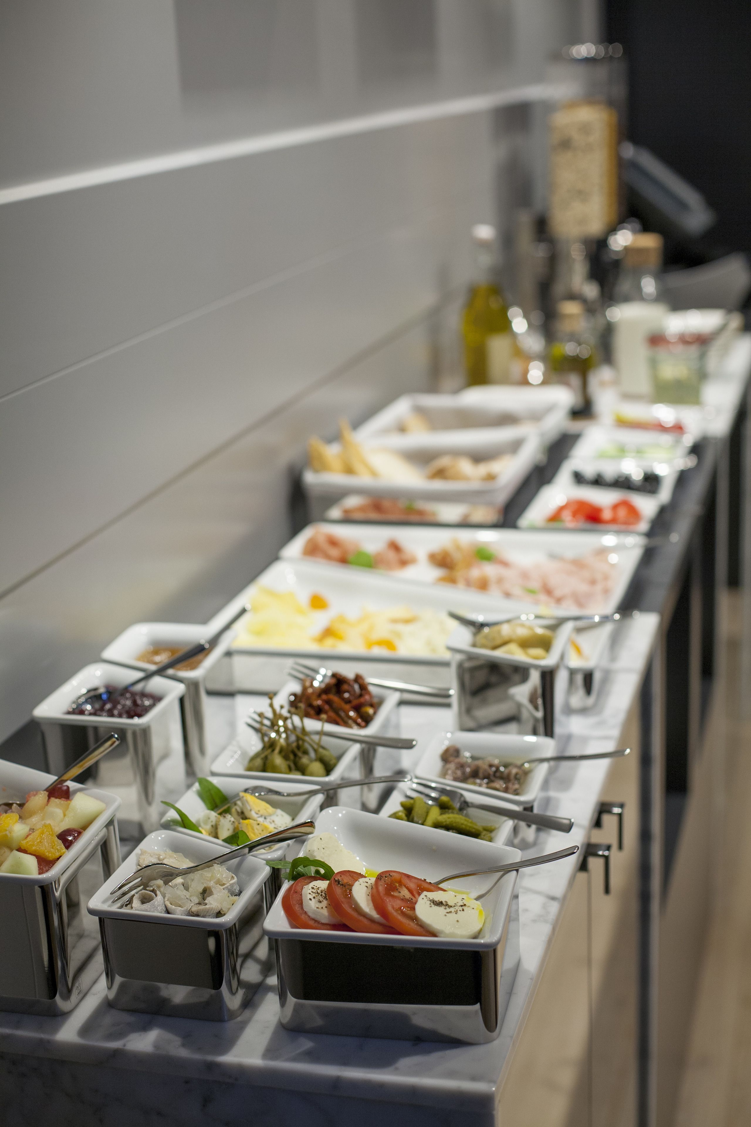 A buffet with various food options in metal containers, including fruits, vegetables, and cheeses.