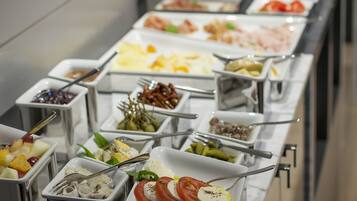 A buffet with various food options in metal containers, including fruits, vegetables, and cheeses.