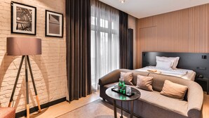 Une chambre d’hôtel moderne avec un lit, un canapé, une petite table avec des boissons et une lampe.