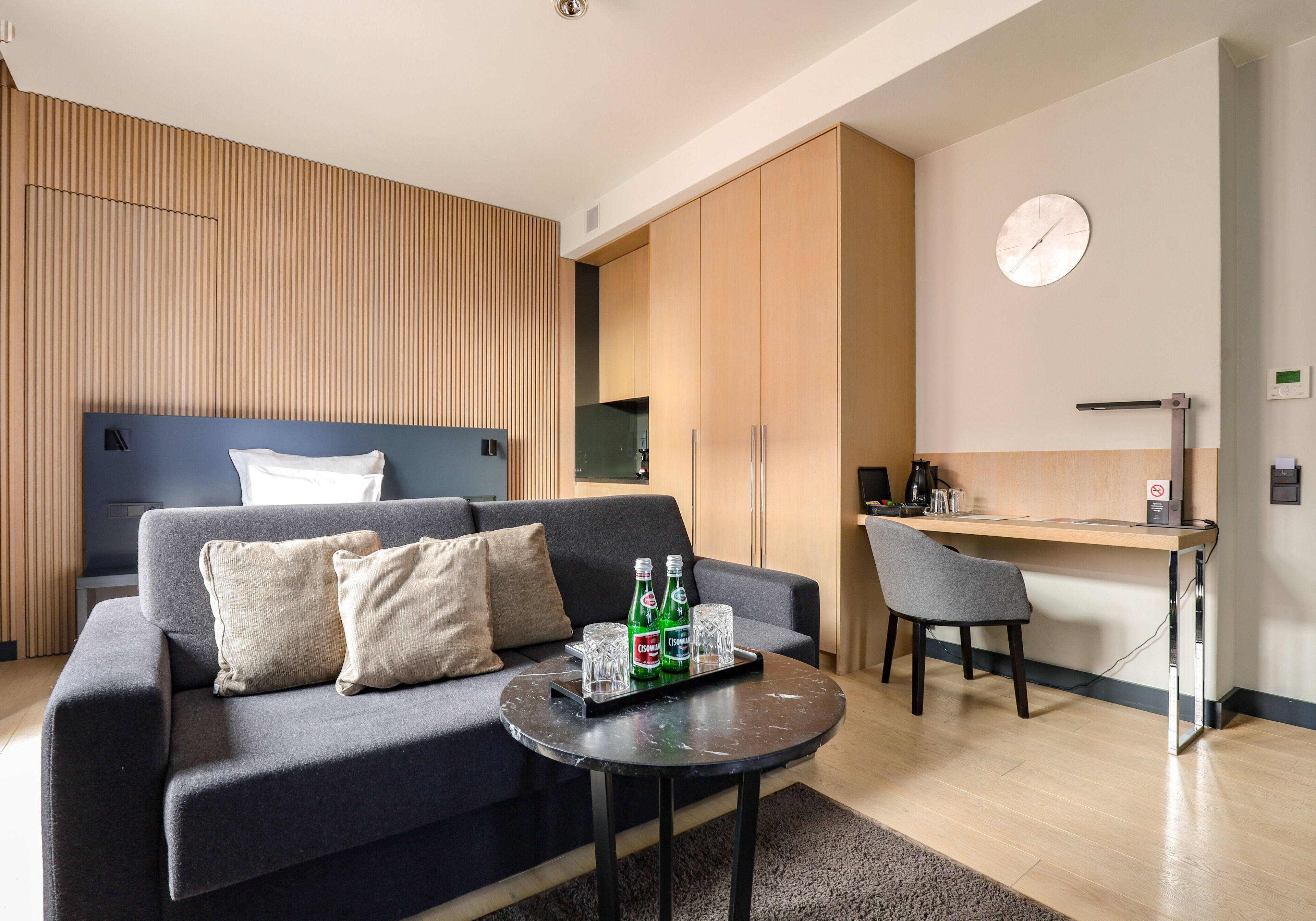 A modern living room with a sofa, a coffee table with drinks, a desk, and a chair.