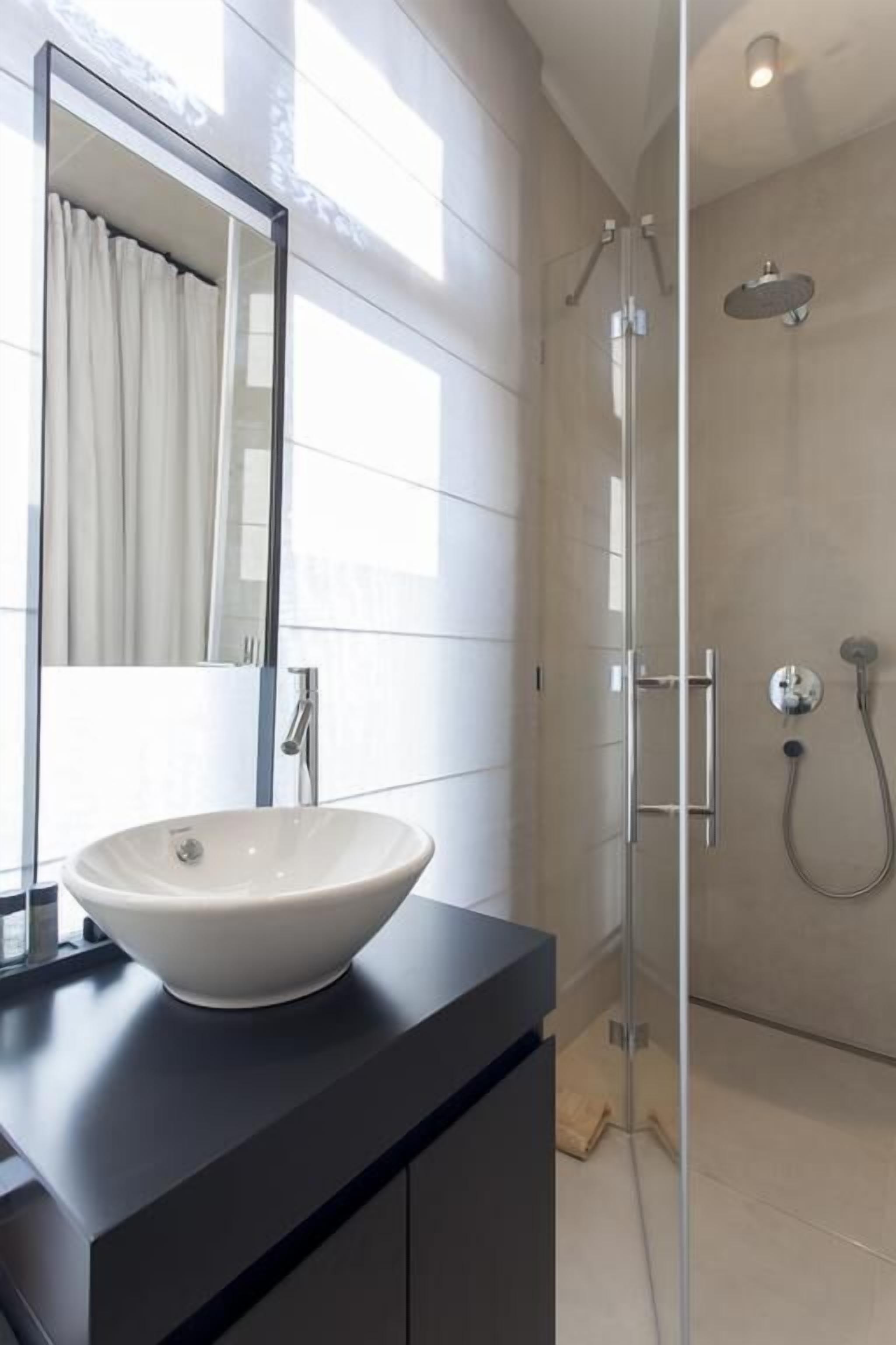 A modern bathroom with a large mirror, a white vessel sink, and a glass-enclosed shower area.