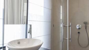 A modern bathroom with a large mirror, a white vessel sink, and a glass-enclosed shower area.